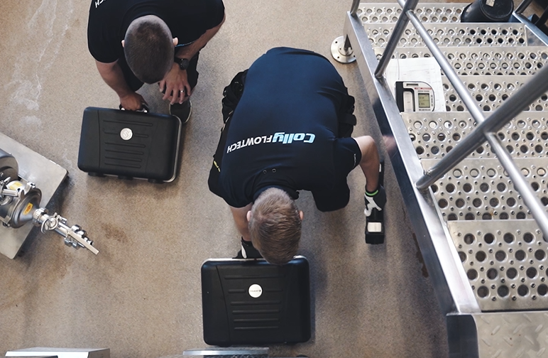 Två tekniker från Colly Flowtech bredvid en svarta utrustningsväskor i en industriell miljö, redo att utföra service eller installation vid en rostfri processanläggning.